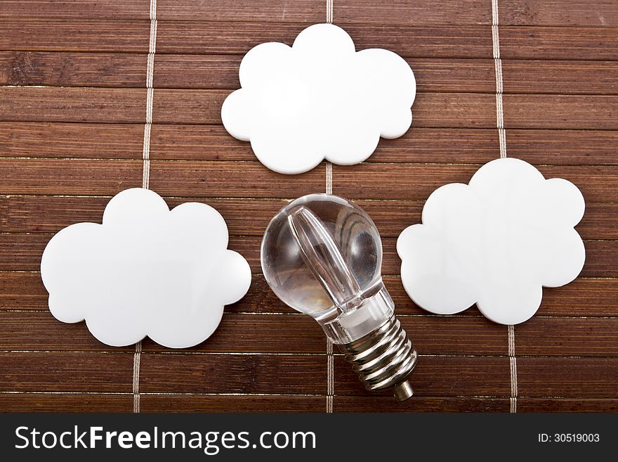 Light bulb with white speech bubbles in a shape of cloud on a wood background.