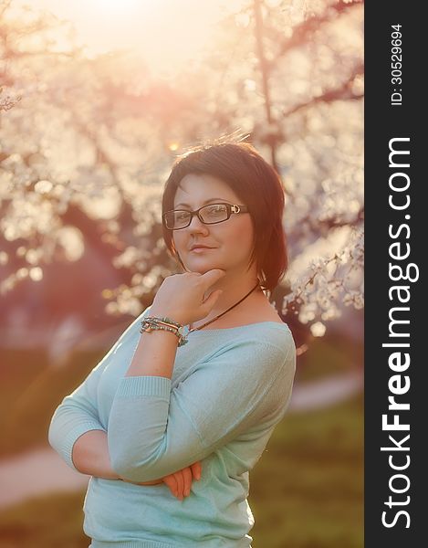 Portrait of a girl with glasses on the background of a flowering tree in spring in the garden