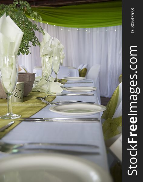 A horizontal image of a wedding table setting with a green theme and depth of field focused on the center of the image.