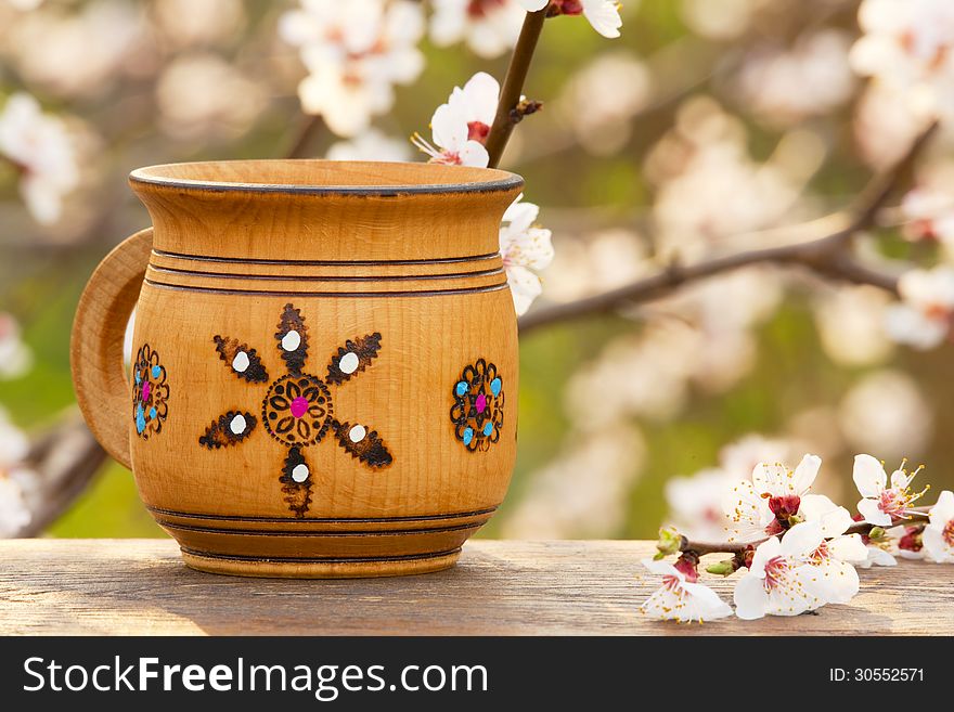 Wooden mug with an ornament in the sunlight on the background a blossoming tree