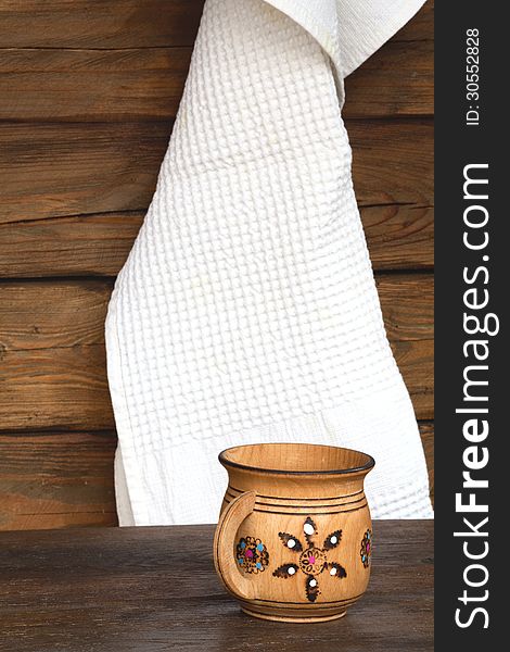 Wooden mug with ornament and a white towel on the background a wooden wall. Wooden mug with ornament and a white towel on the background a wooden wall