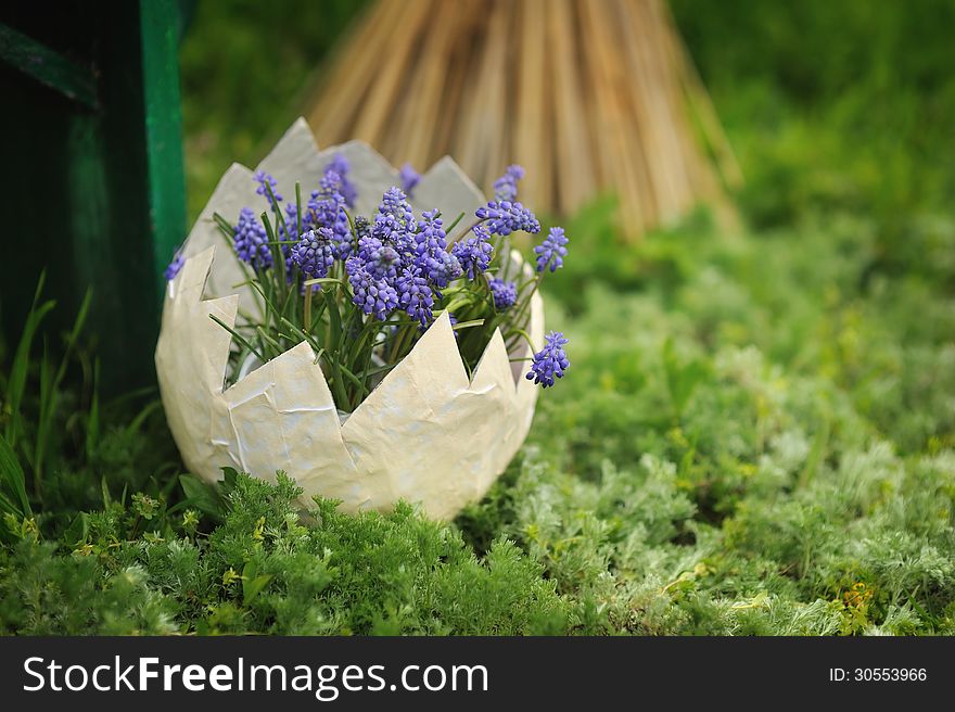 On the green grass in the pot as a white egg with blue flowers. On the green grass in the pot as a white egg with blue flowers