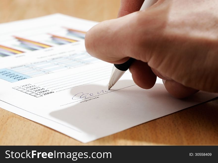 Man's hand signing document on the table