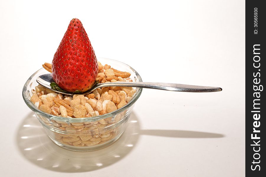 A strawberry on a spoon on a glass bowl of cereal. A strawberry on a spoon on a glass bowl of cereal.