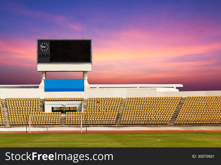 Rows of orange seats on the stadium with scoreboard displaying clock above them