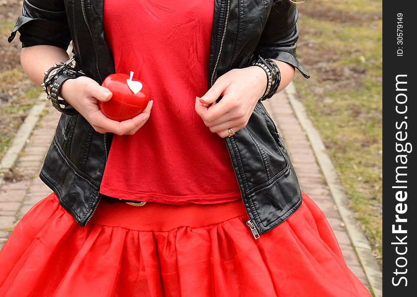 A red apple in a hand of a girl in a red dress with black jacket