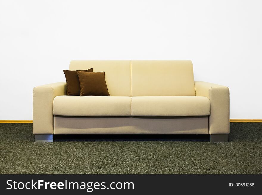 Beige modern sofa with brown cushions before white wall.
