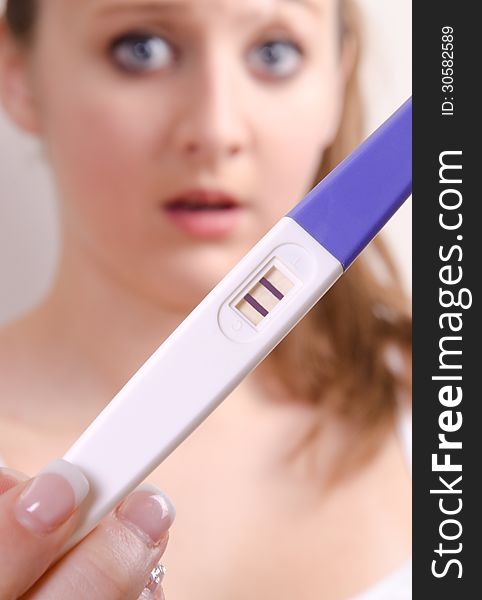 Cute girl is showing her positive pregnancy test. The girl is surprised.