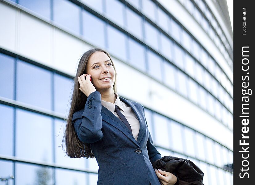 Portrait of pretty young business woman talking on phone near building, talking