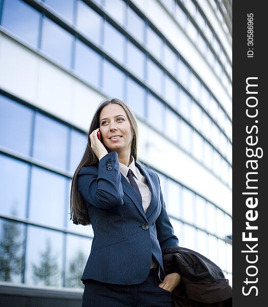 Portrait of pretty young business woman talking on phone near building, talking