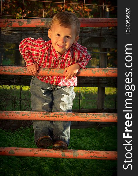 A Smiling Young Boy Climbs Corral Fence