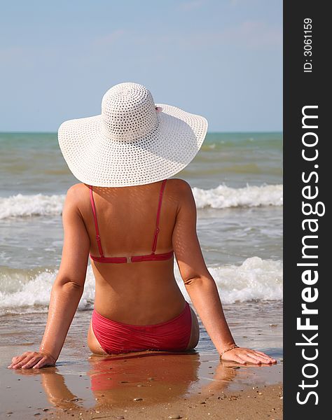 Young woman sits on the sand on the edge of the sea