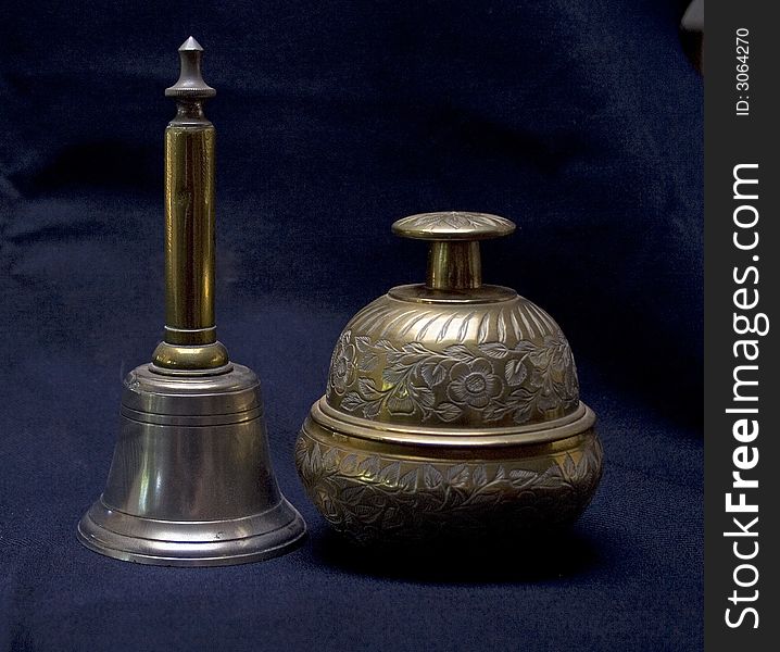 The two brass bells contrast in style. The one is upright sith simple lines, the other is rotund with a flowery motif.