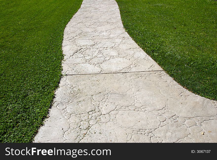 Textured cement pathway diminishing through lush green grass