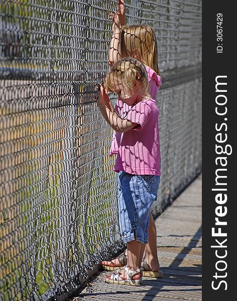 Two sisters in pink shirts looking through chain link fence. Two sisters in pink shirts looking through chain link fence