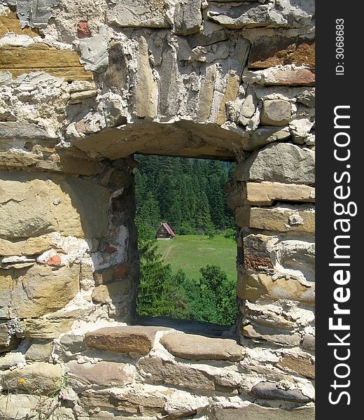 Window in a stone wall with view to forest and a small house