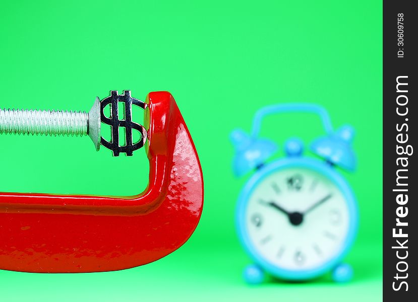 A silver Dollar symbol placed in a red clamp with a pastel green background, with a light blue alarm clock in the background indicating the pressure on dollar. A silver Dollar symbol placed in a red clamp with a pastel green background, with a light blue alarm clock in the background indicating the pressure on dollar.