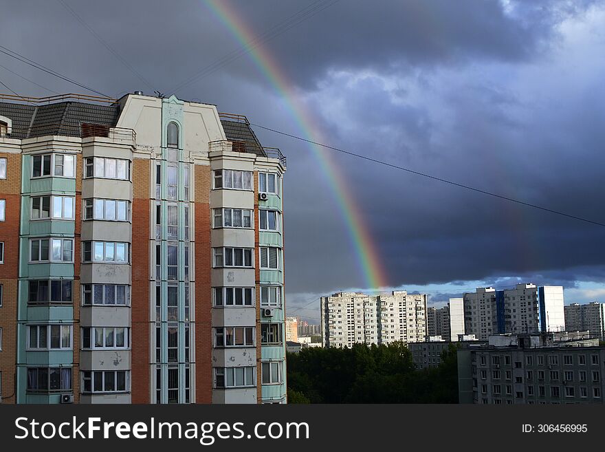 Landscape with a panel high-rise house on a dark sky with a rainbow. Double rainbow in the dark sky. A storm cloud over the city.