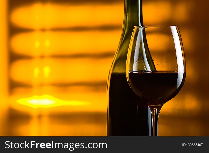 Bottle and glass with red wine on a yellow background