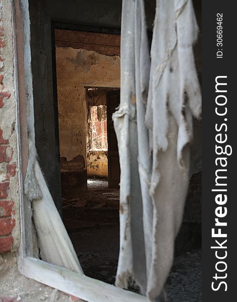 View of the inside of an abandoned building, a shabby curtain is in the front, in the background rooms with scrapped walls