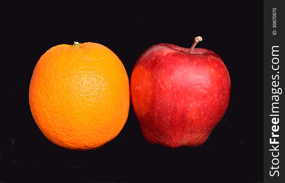 An apple and an orange on a black background. An apple and an orange on a black background.
