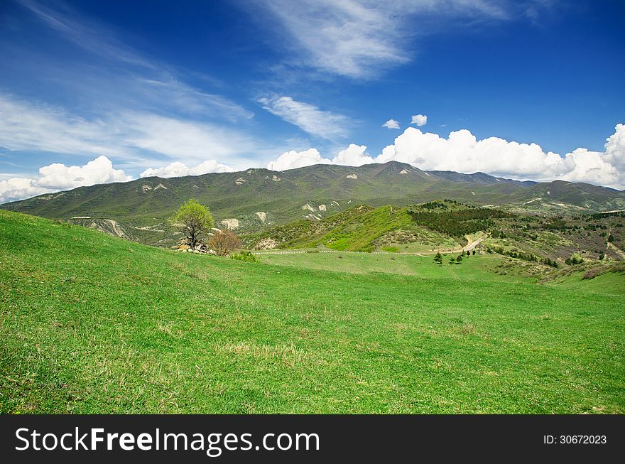 Green meadow and mountains in the background of the beautiful blue sky with clouds. Green meadow and mountains in the background of the beautiful blue sky with clouds