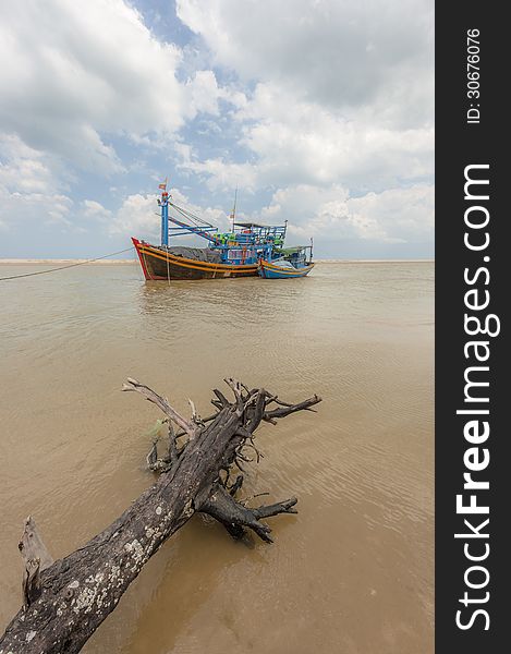 Fishing boats and wood stick at the shore-line with the cloudy sky at background