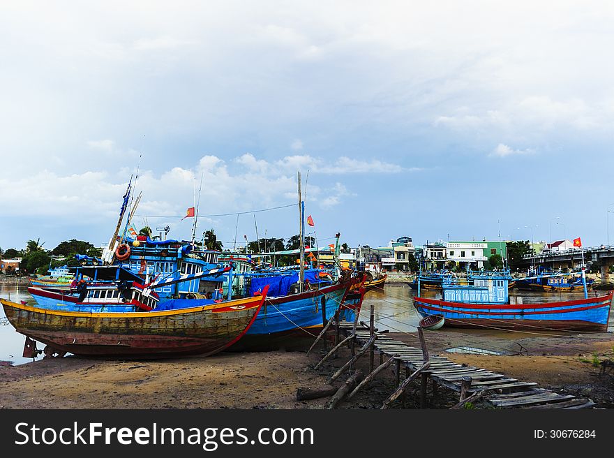 Fishing boats in harbor with the jetty at foreground and cloudy sky at background