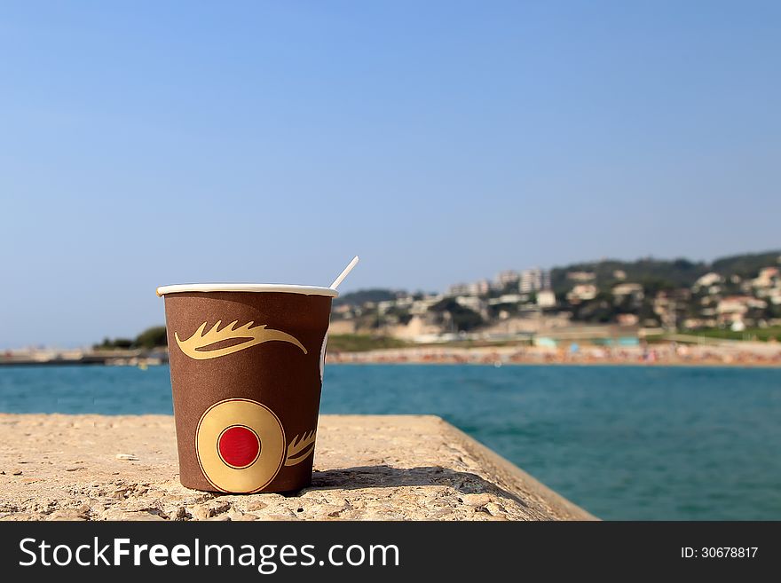 Paper cup of coffee on the beach with sea as a background.