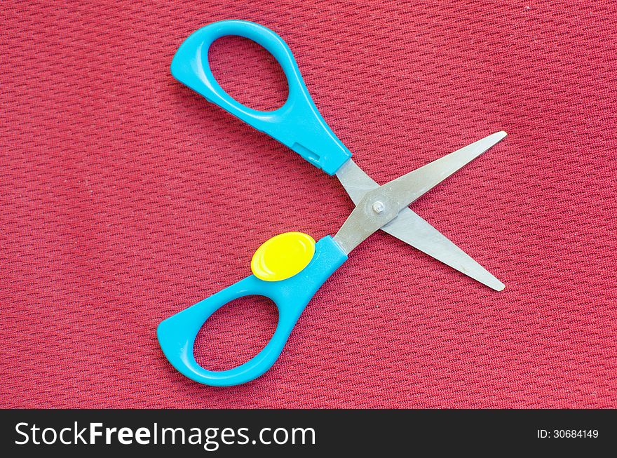 Opened colorful scissor on red textile background