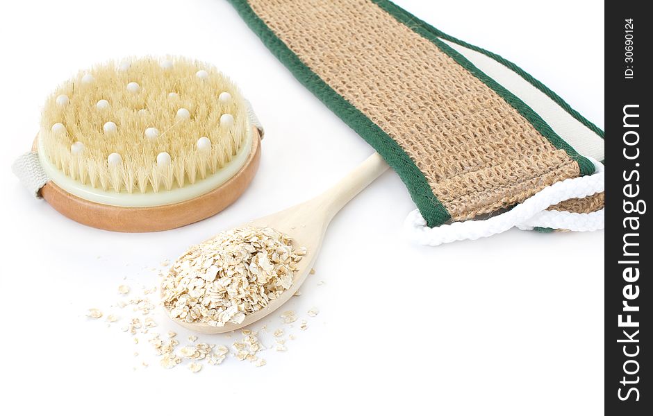 A spa composition, massage brush, oatmeal in the wooden spoon and brush on white background. A spa composition, massage brush, oatmeal in the wooden spoon and brush on white background