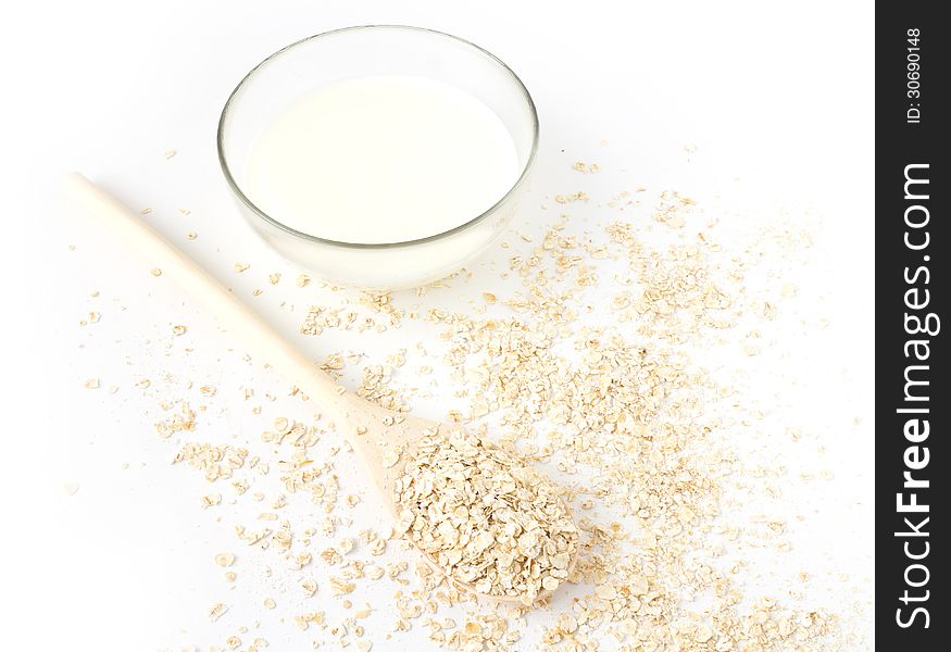 Oatmeal in the wooden spoon and milk on white background