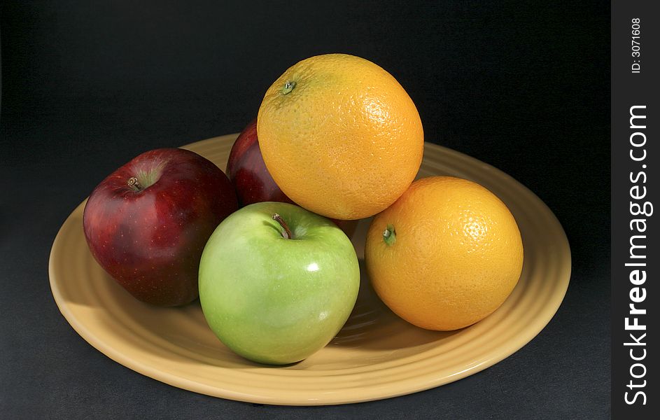 Apples and oranges mixed fruits on yellow plate with dark background. Apples and oranges mixed fruits on yellow plate with dark background