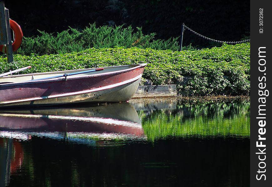 A row boat parked on the shore of a pond.