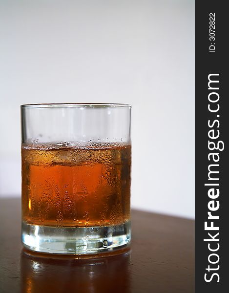 The misted over glass of whisky with an ice on a table