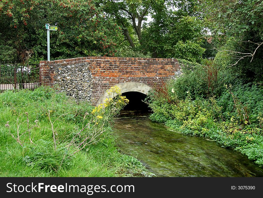 Stream flowing under a Brick and Flint Bridge in a water meadow in rural England. Stream flowing under a Brick and Flint Bridge in a water meadow in rural England