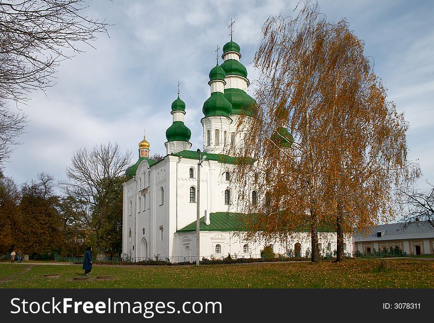 Old woman praying near of Orthodoxy Christianity church with yellow autumn tree