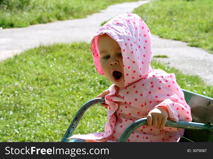 Little baby sitting on the carousel and yawning. There is green grass and crossroad on the backstage. Little baby sitting on the carousel and yawning. There is green grass and crossroad on the backstage