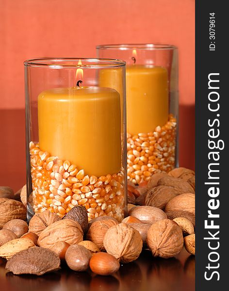 A candle in an autumn setting with corn and nuts