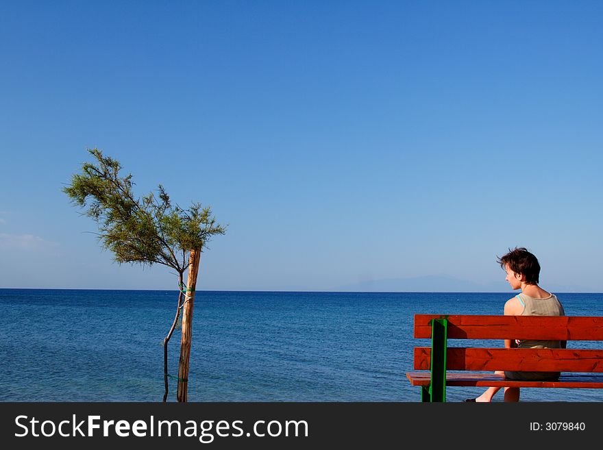 Young girl on a banch on the coast with a small tree