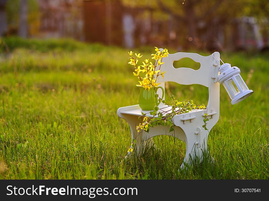 White wooden chair with flowers and white decorative lantern in the sunset light. White wooden chair with flowers and white decorative lantern in the sunset light