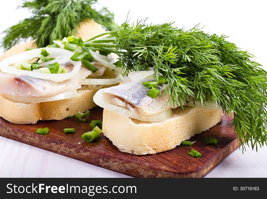 Sandwiches of white bread with herring, onions and herbs on wooden board