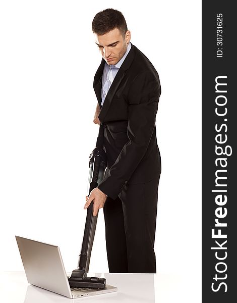 Serious and attractive young businessman vacuum cleans his laptop. Serious and attractive young businessman vacuum cleans his laptop