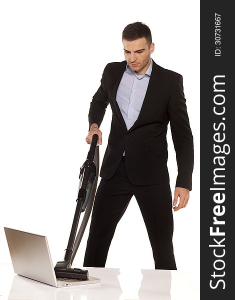 Serious and attractive young businessman vacuum cleans his laptop. Serious and attractive young businessman vacuum cleans his laptop