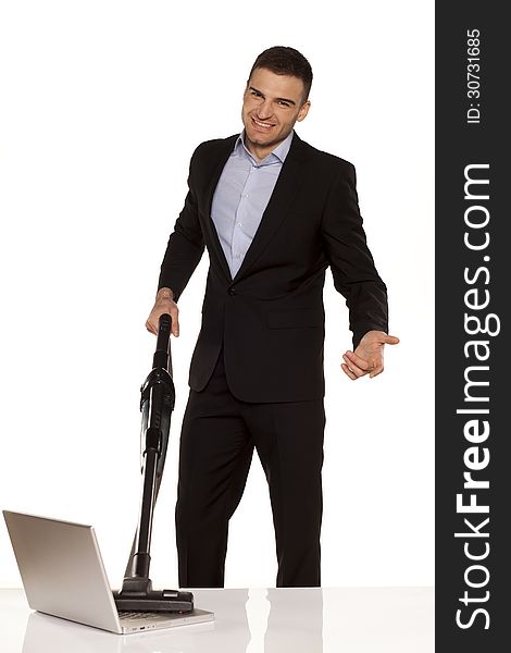 Smiling and attractive young businessman vacuum cleans his laptop. Smiling and attractive young businessman vacuum cleans his laptop
