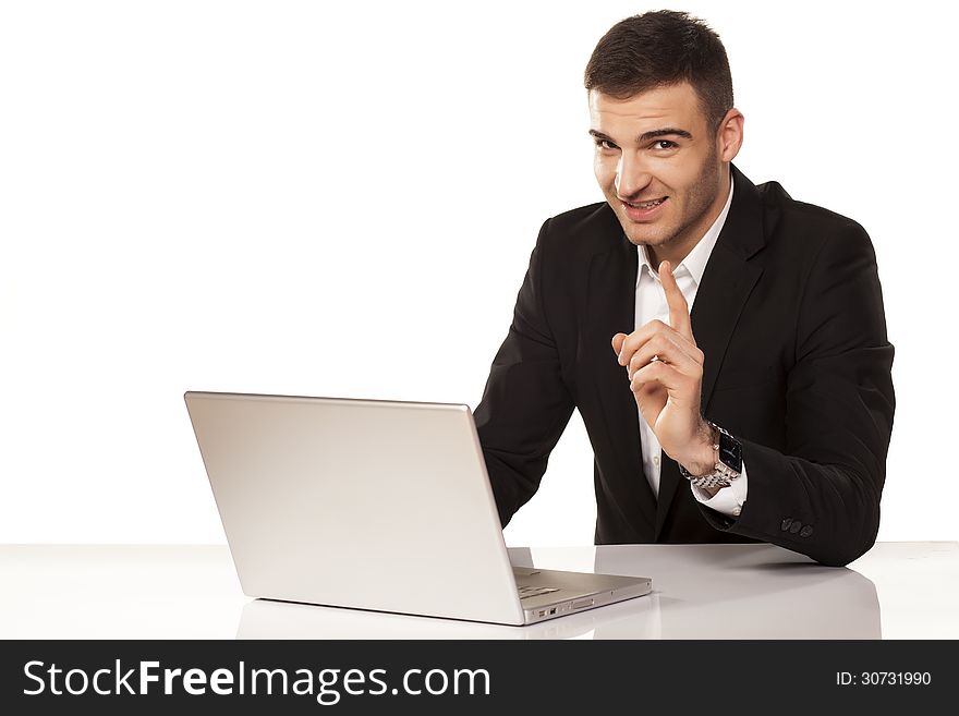 Smiling young and attractive businessman shows his finger up behind his laptop. Smiling young and attractive businessman shows his finger up behind his laptop