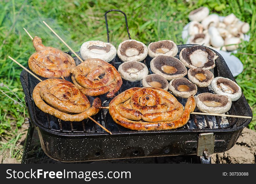 Champignon mushrooms and sausages cooking on barbecue in garden. Champignon mushrooms and sausages cooking on barbecue in garden.