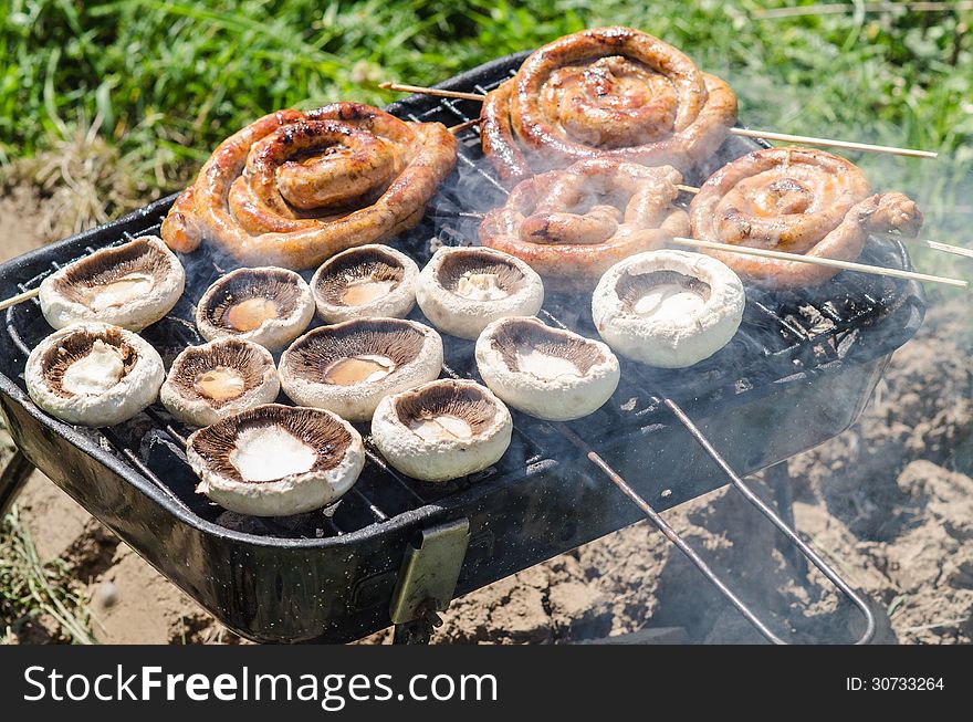 Champignon mushrooms and sausages cooking on barbecue in garden. Champignon mushrooms and sausages cooking on barbecue in garden.