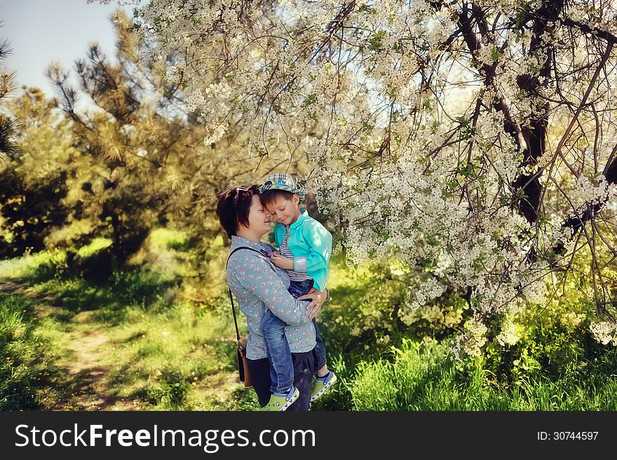 In nature in a lush garden a little boy in the blue shirt in the hands of mother. In nature in a lush garden a little boy in the blue shirt in the hands of mother