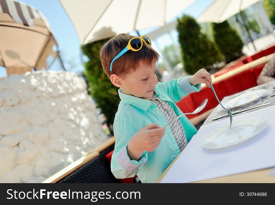 Stylish little boy with sunglasses sitting at a table in a restaurant. Stylish little boy with sunglasses sitting at a table in a restaurant